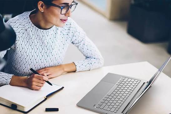 mujer haciendo busqueda en una laptop y anotaciones en un cuaderno.